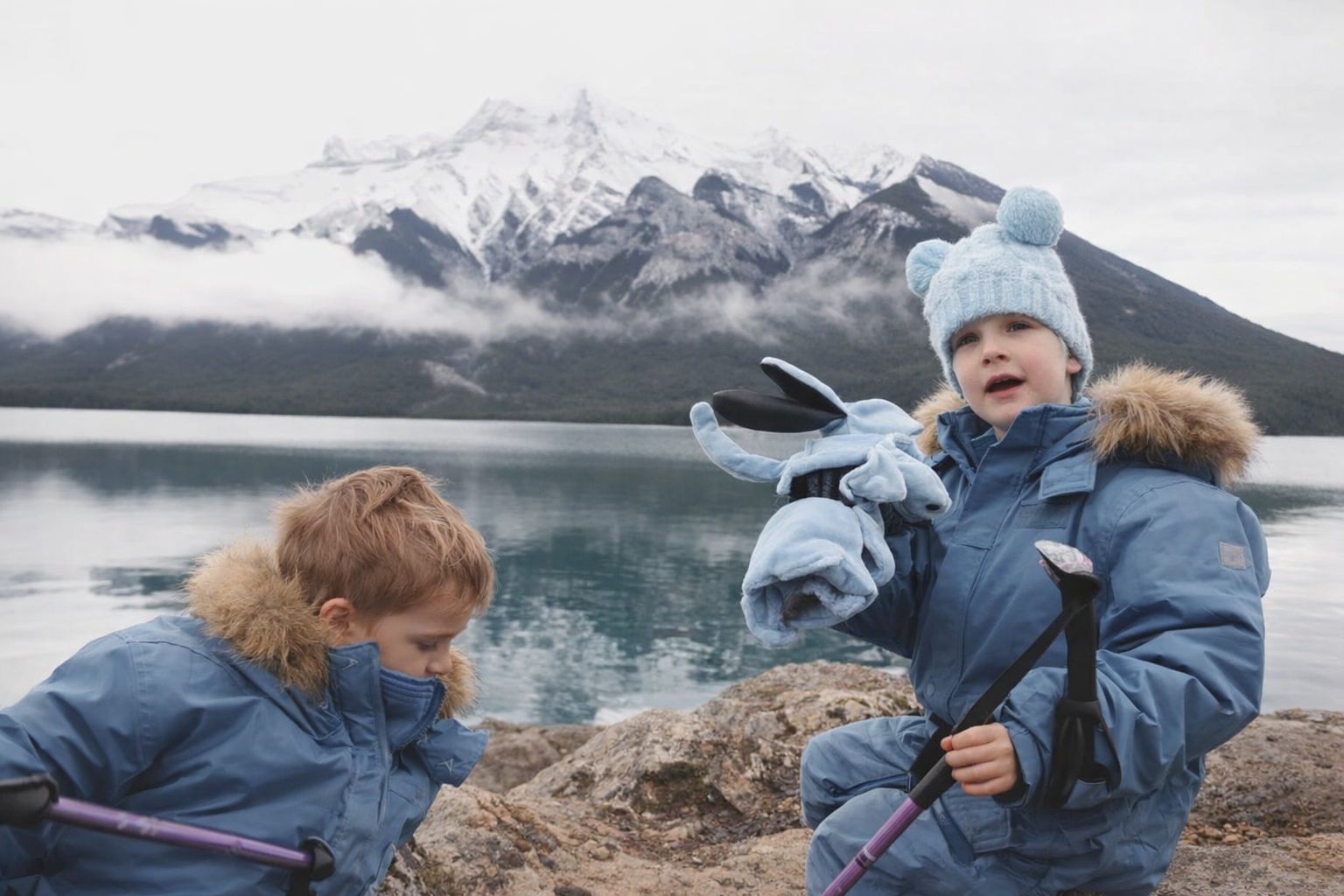 Dzieci w niebieskich kurtkach zimowych nad jeziorem w górach.